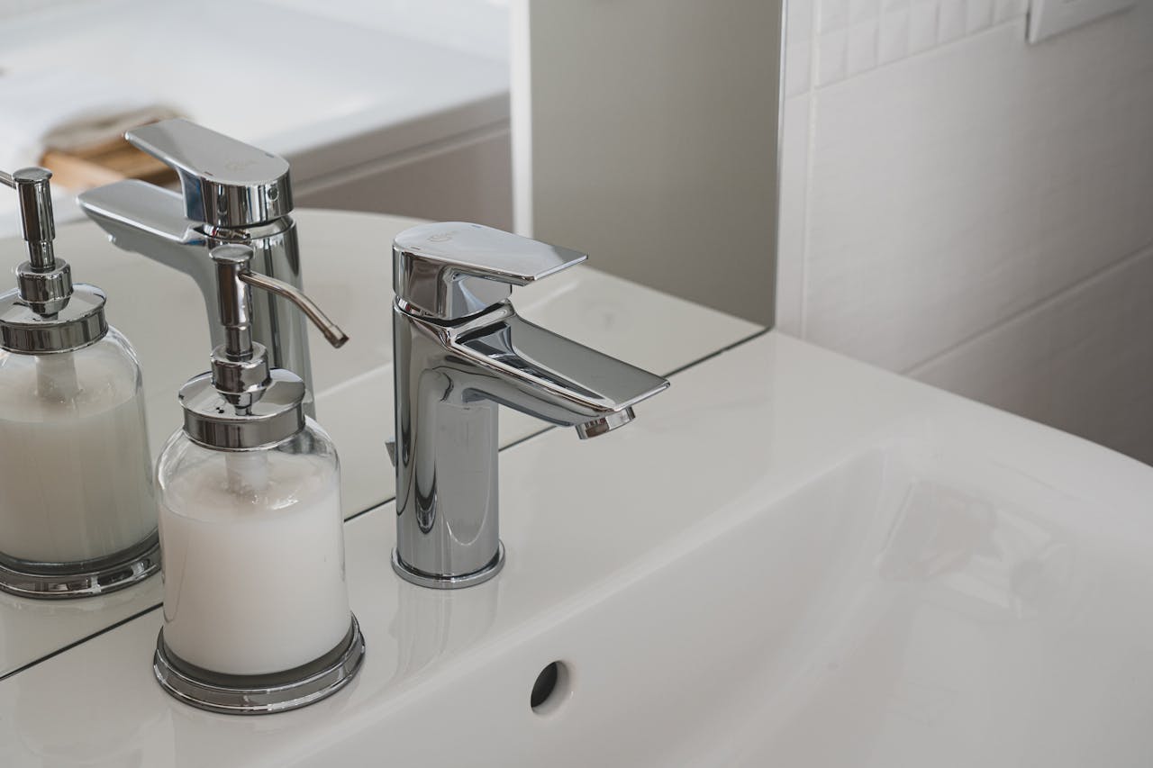 gallery-05 A sleek chrome faucet and soap dispenser on a pristine white sink in a modern bathroom setting.